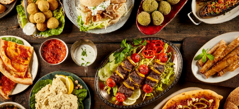 Display of Mediterranean dishes on a wooden tabe including falafel, kebabs and hummus