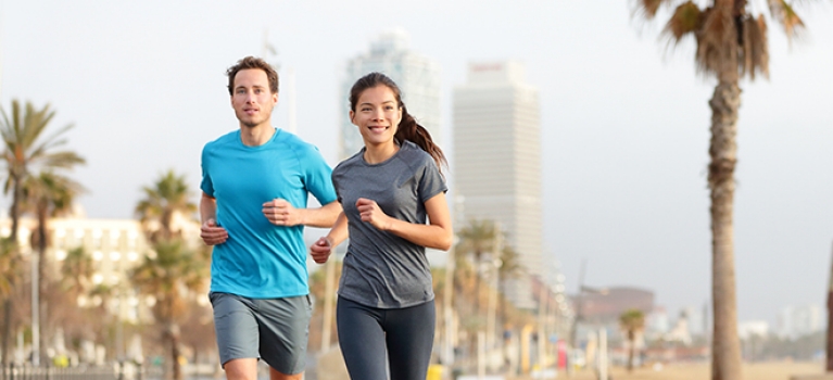 Caucasian male and Asian female jogging on Barcelona Beach in Barcelona, Spain