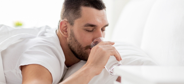 Young man drinking water while lying in bed