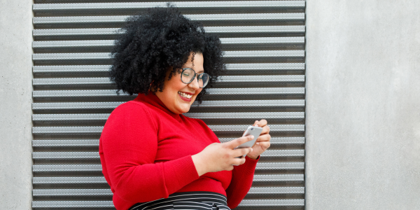A woman is smiling while checking her smartphone.
