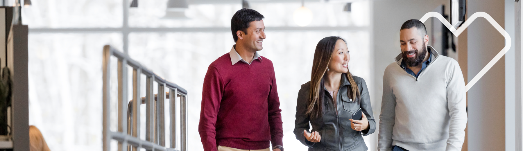 Three people talking while walking on a hall with the Aetna heart in the background.