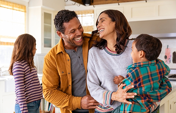 A happy family together. A man smiling while holding his wife and son, with a small girl in the background.