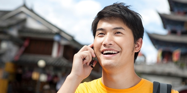 An asian young man talking on the phone while traveling.