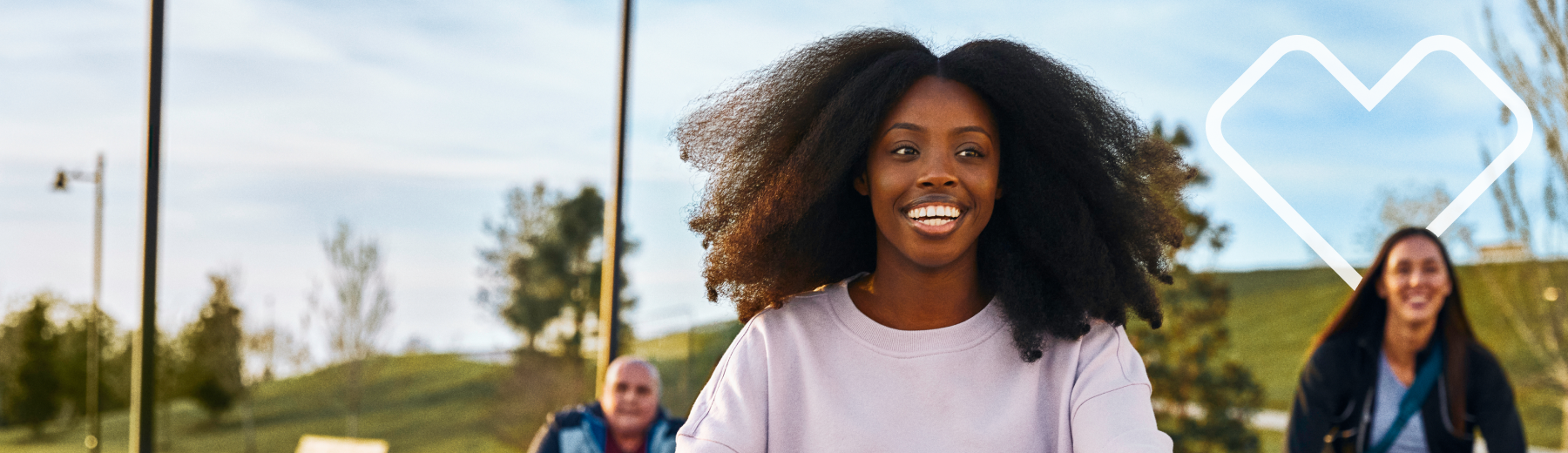 Two girls smiling, one behind the other, in a meadow with the Aetna heart in the background.